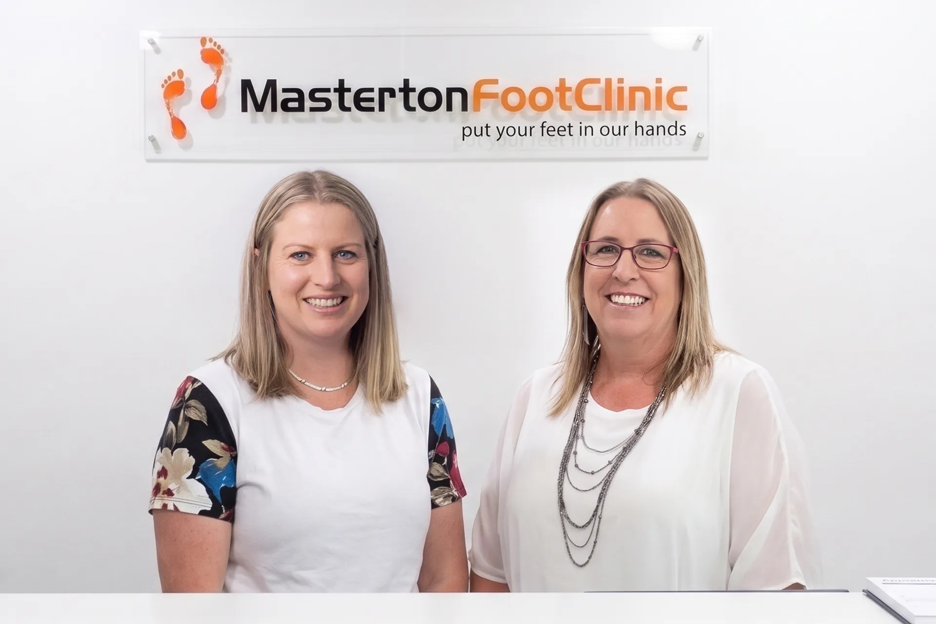 Jannah and Sarah smiling behind the reception counter at Masterton Foot Clinic